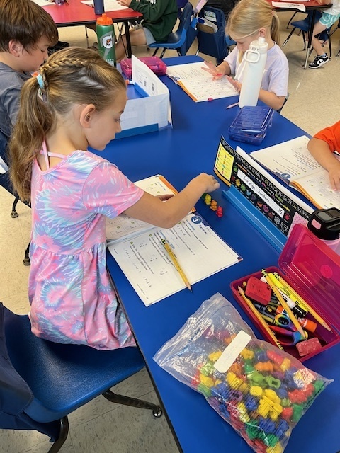 A young girl uses small bears to help count through problems in her math workbook 
