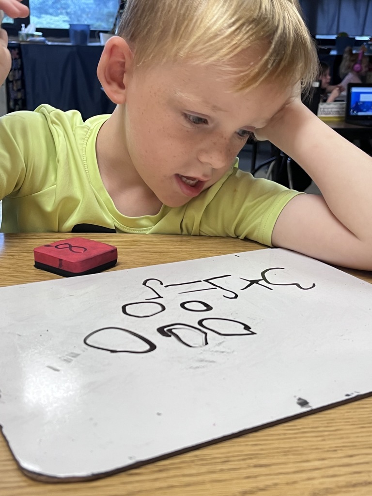 A young boy works out a math problem in a small white board 
