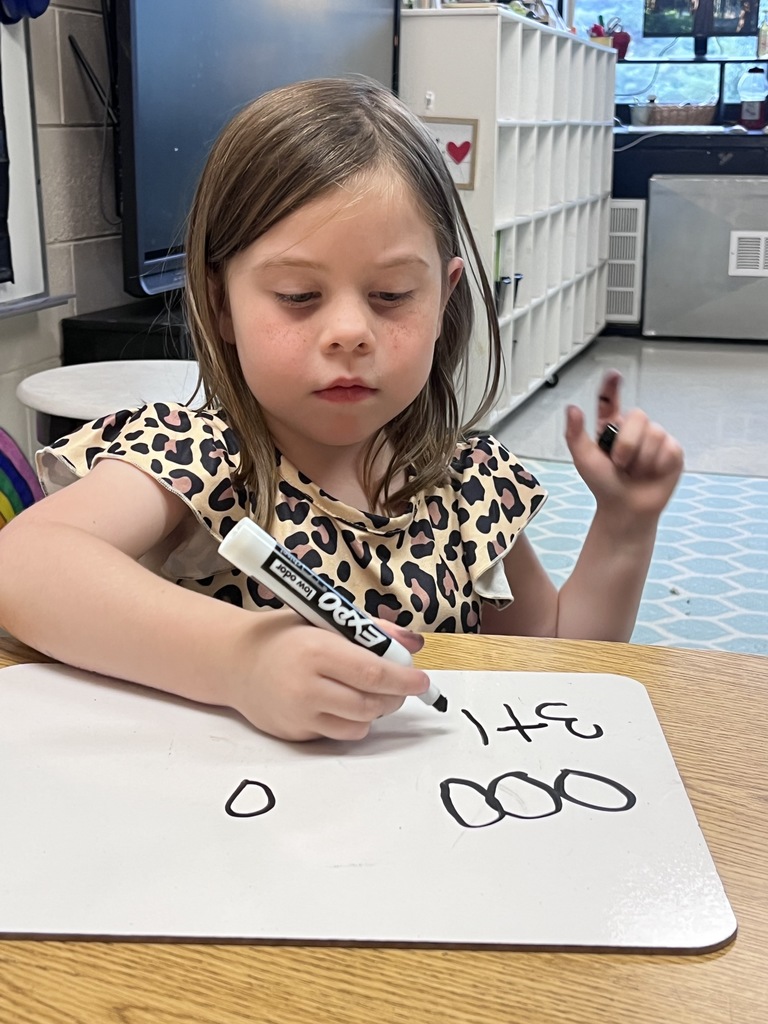 A young girl works out a math problem on a white board 