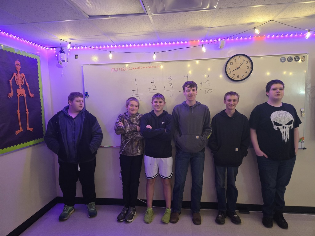 6 high school boys stands in front of a large classroom whiteboard with math equations written on it. 