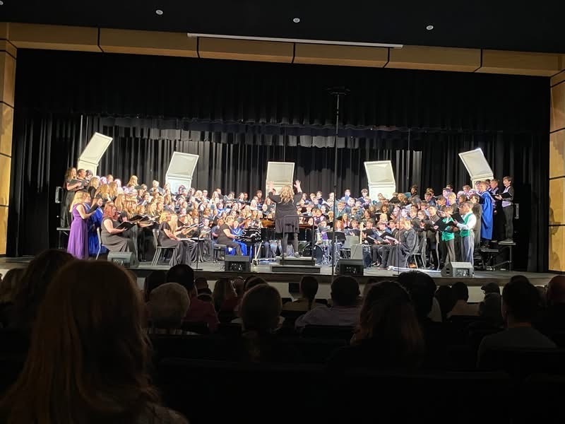 Picture of a large choir made up of area high school students.  Choir is being directed by a woman wearing black.  