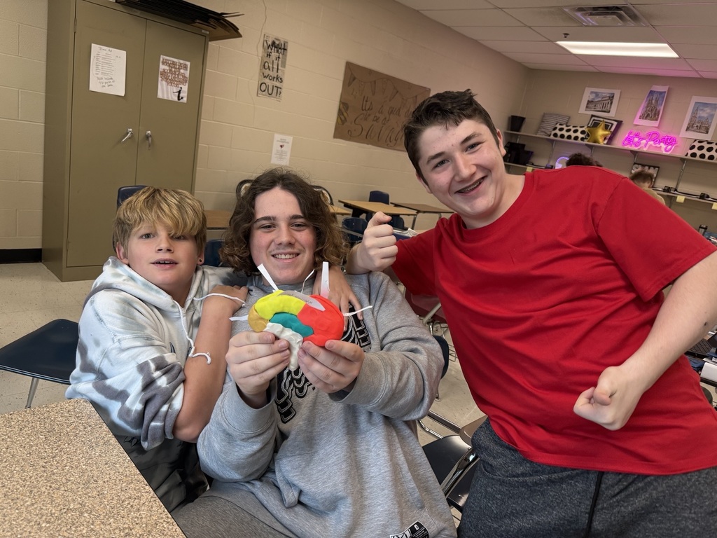 Three smiling students hold up their completed Play-Doh brain model in a classroom, showing off their work.