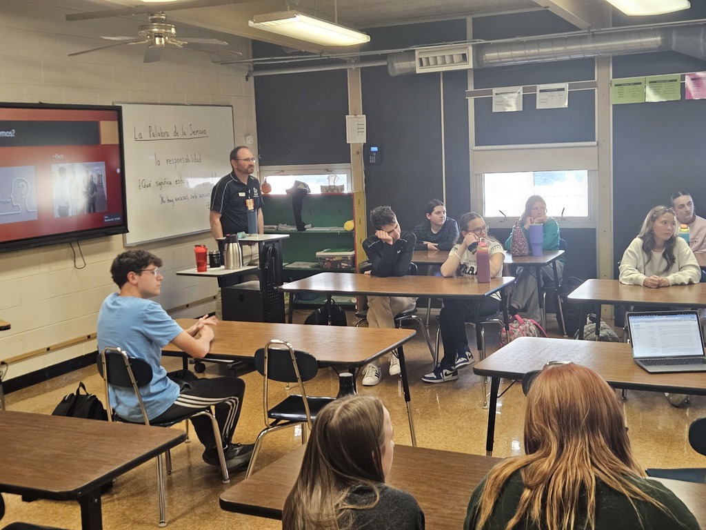 Students watch and listen as the guest speaker near the presentation screen discusses opportunities related to language and healthcare.