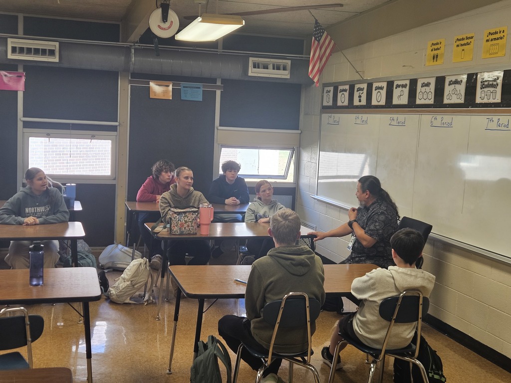 One of the guest speakers sits at the front of the room, engaging a small group of students in discussion.
