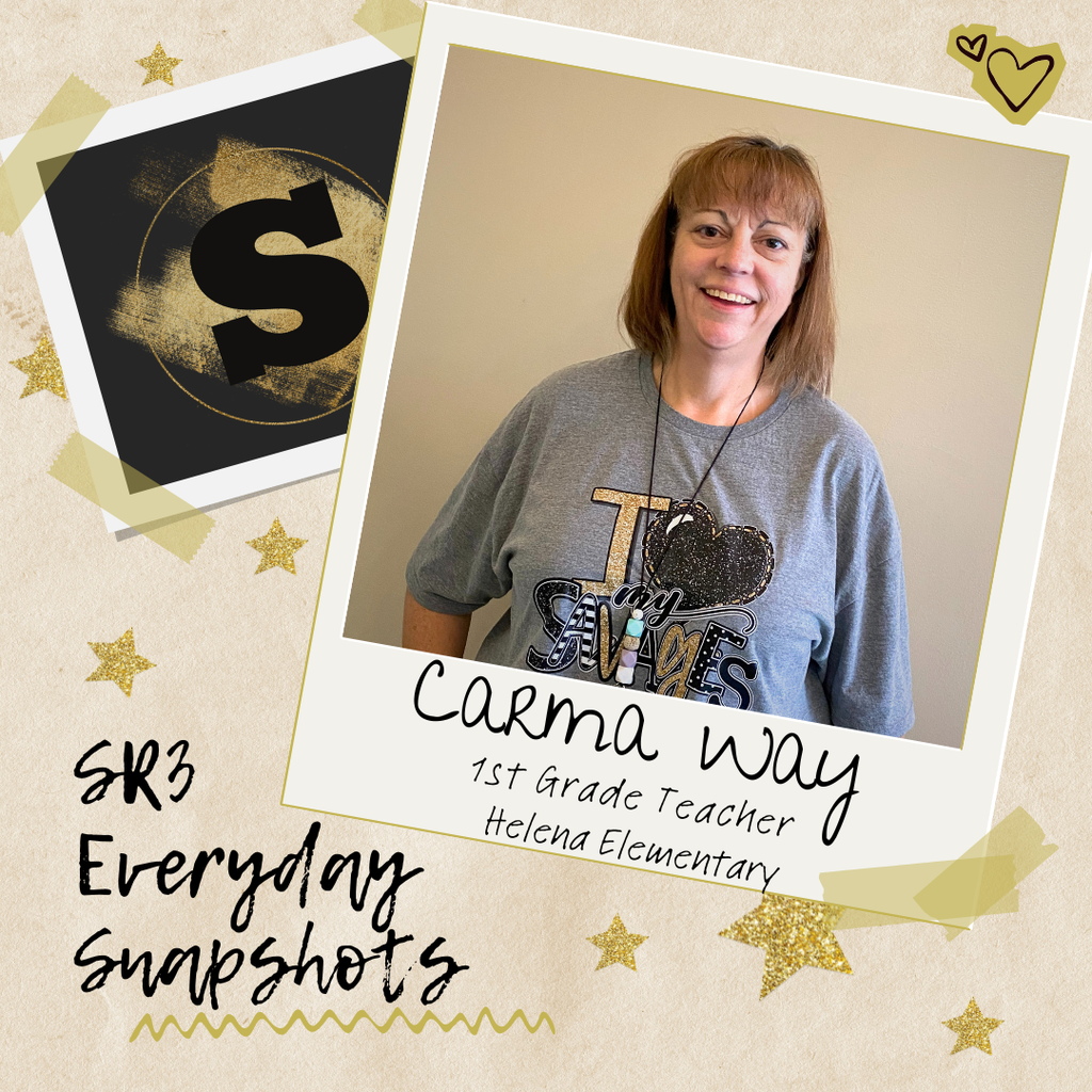 First grade teacher Carma Way stands against a beige wall wearing an ‘I love my Savages’ shirt, smiling at the camera.