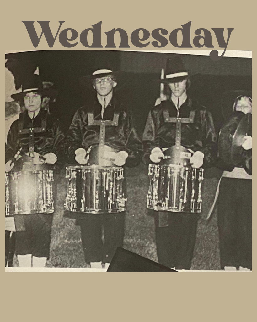 Vintage black-and-white photo of four high-school marching band drummers standing in uniform with tall hats and shiny snare drums. The word ‘Wednesday’ is styled across the top.