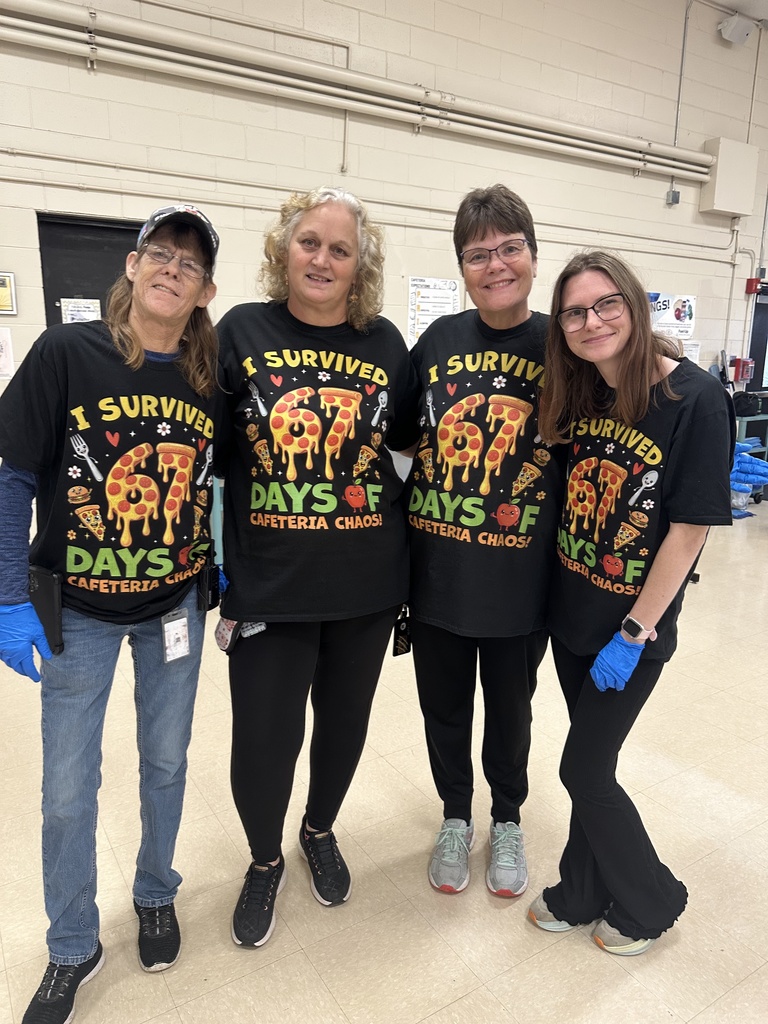 Four Minnie Cline lunch duty staff wearing matching ‘I Survived 67 Days of Cafeteria Chaos’ shirts, standing together and smiling.