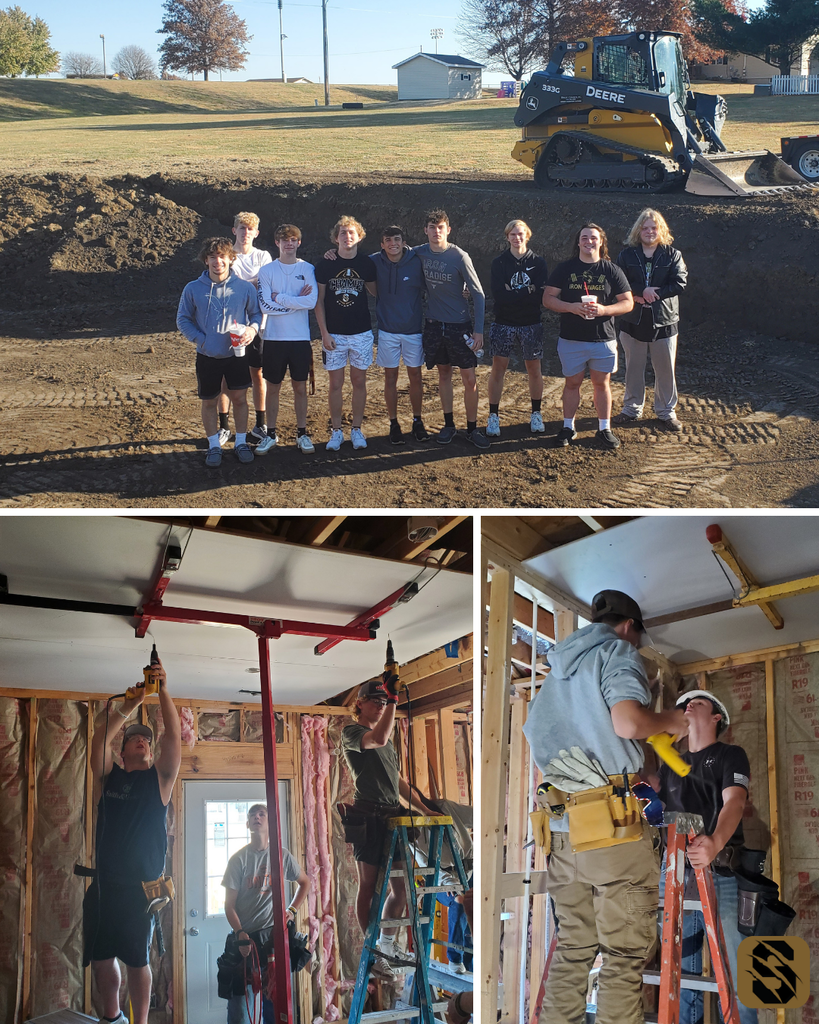 Building Trades students standing in a dug foundation and working on ceiling panels inside the framed house.