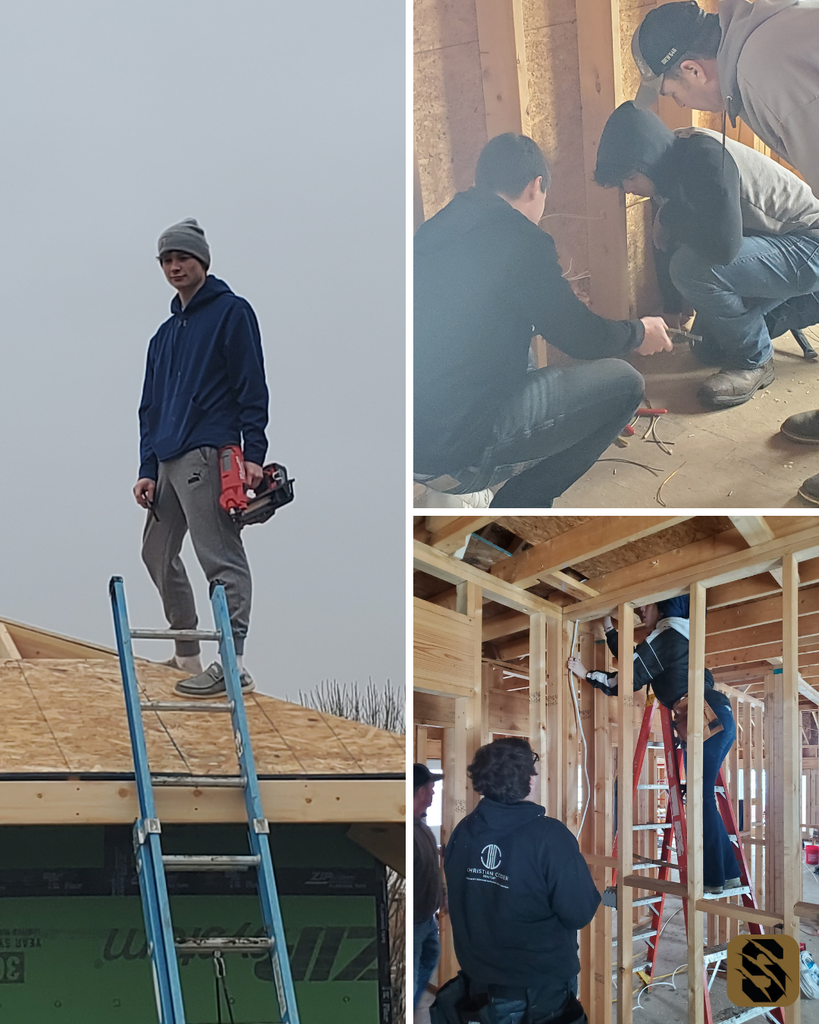 Students installing wiring and drywall inside the framed house, with one student standing on the roof holding a nail gun.