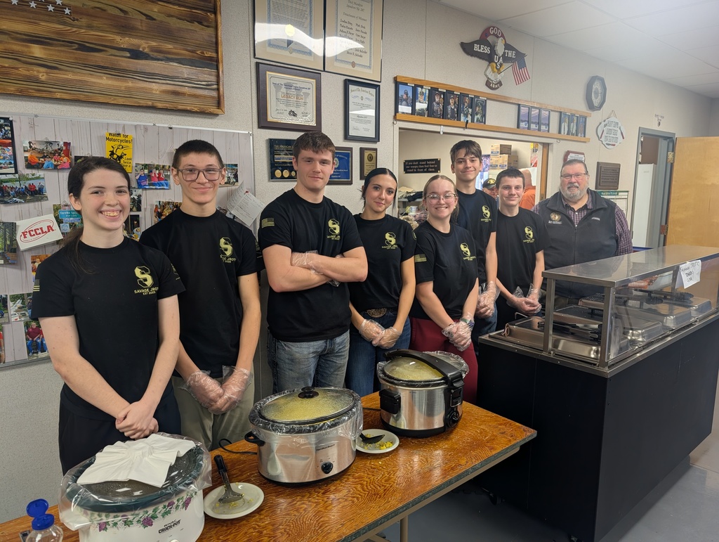 Eight Savannah High School JROTC cadets stand behind a serving table at the American Legion, wearing black JROTC shirts and food-service gloves.