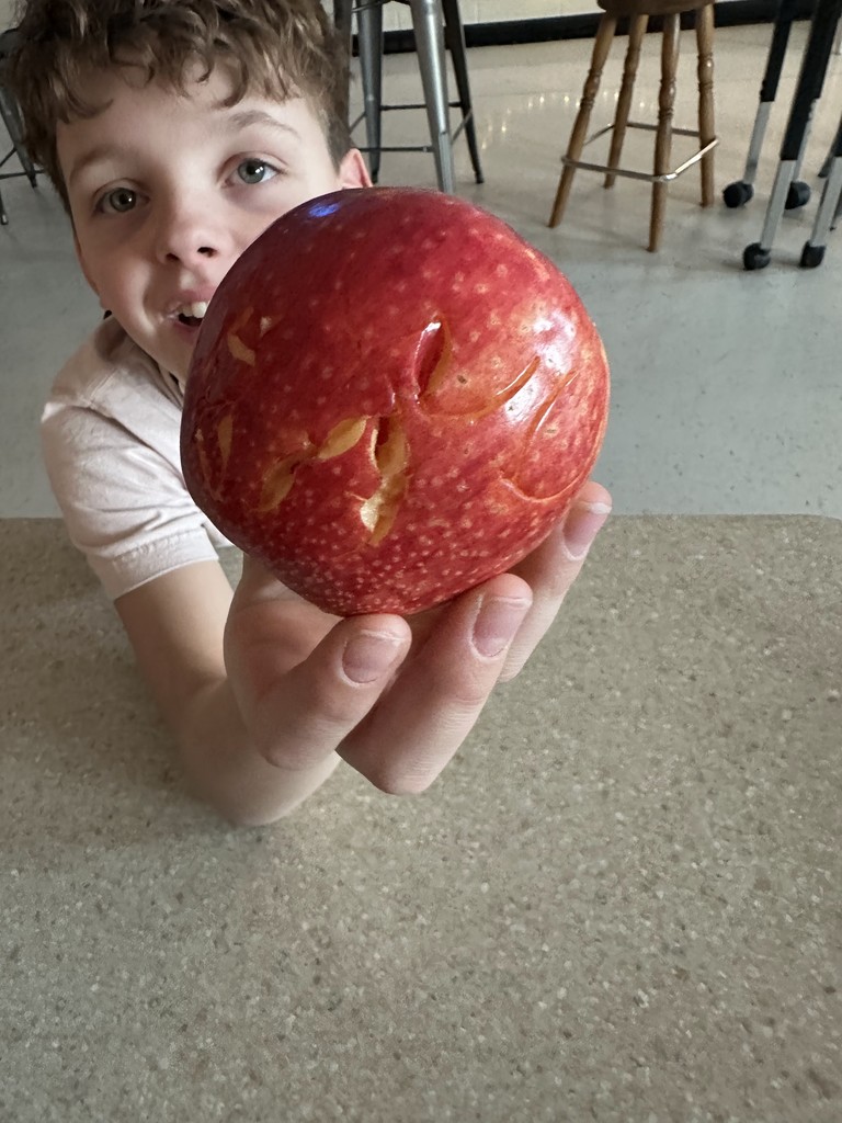 A student holding a red apple with carved markings, showing the symbols cut into the surface.