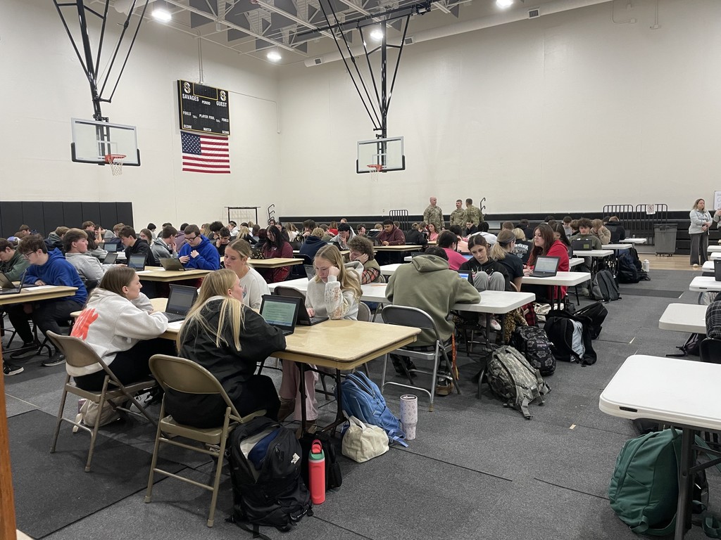 Savannah High School juniors seated at tables in the gym, completing the ASVAB online assessment on laptops.