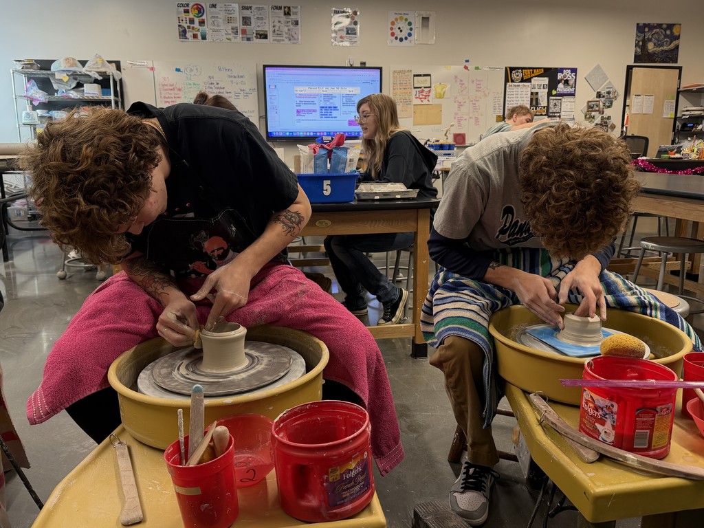 Two students shape small clay forms on pottery wheels during 3-D art class.