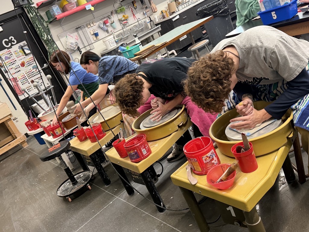 Students lean over pottery wheels, shaping clay bowls in a 3-D art classroom.