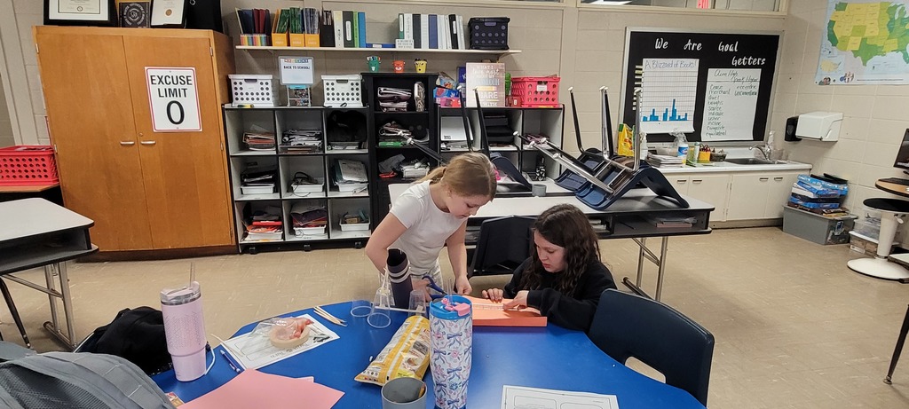 Two students cut and assemble materials at a table during a hands-on STEM activity.