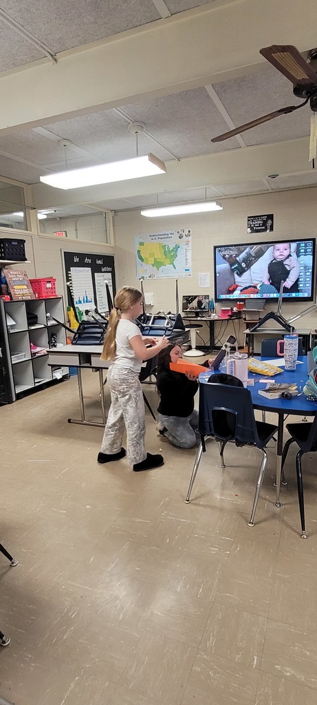 Fourth grade students build a tall paper roller coaster structure in a classroom.