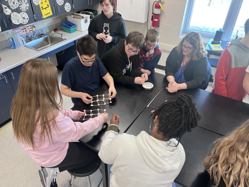 Students gather around a lab table constructing three-dimensional atomic structures.