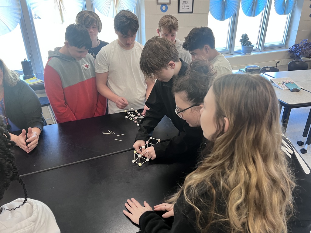 Group of eighth grade students build cube-shaped molecular models using marshmallows and toothpicks in a science classroom.