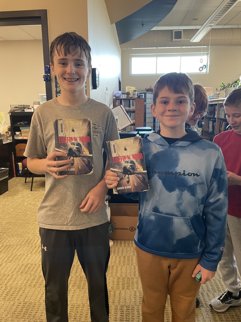 Two middle school boys in the library hold copies of The Final Hour and smile.