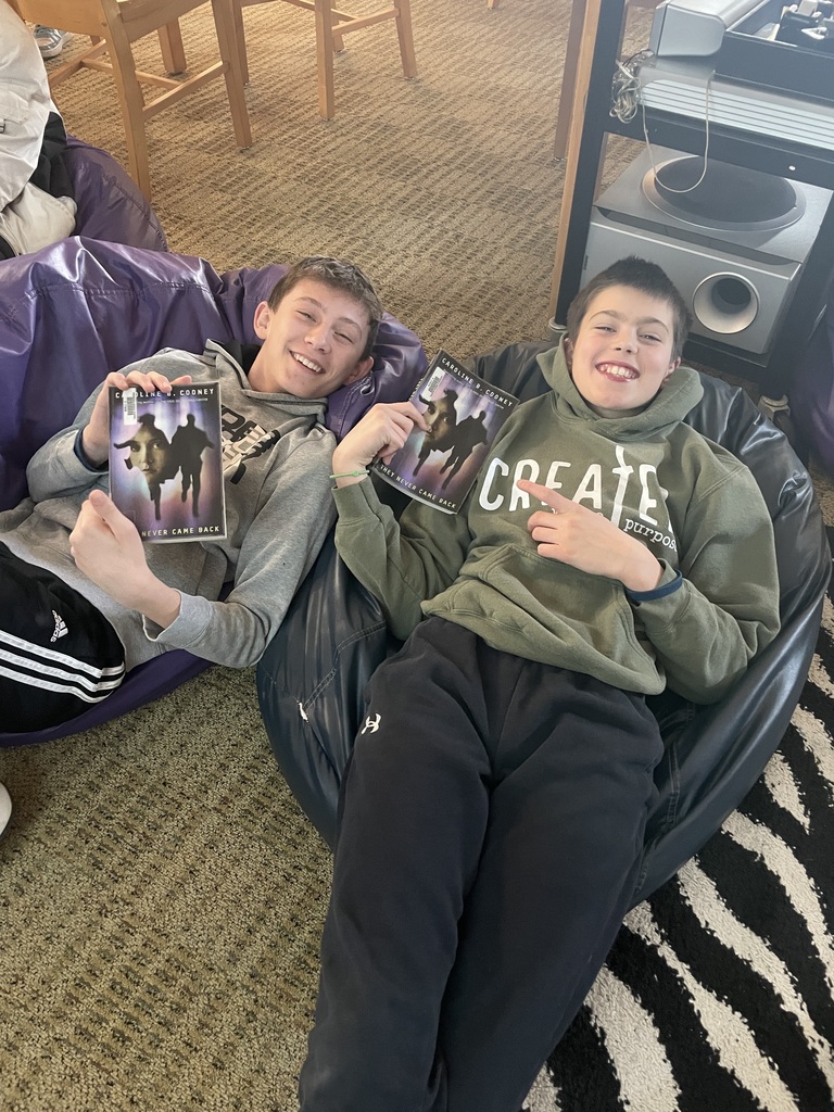 Two middle school boys relax on bean bags holding copies of They Never Came Back.