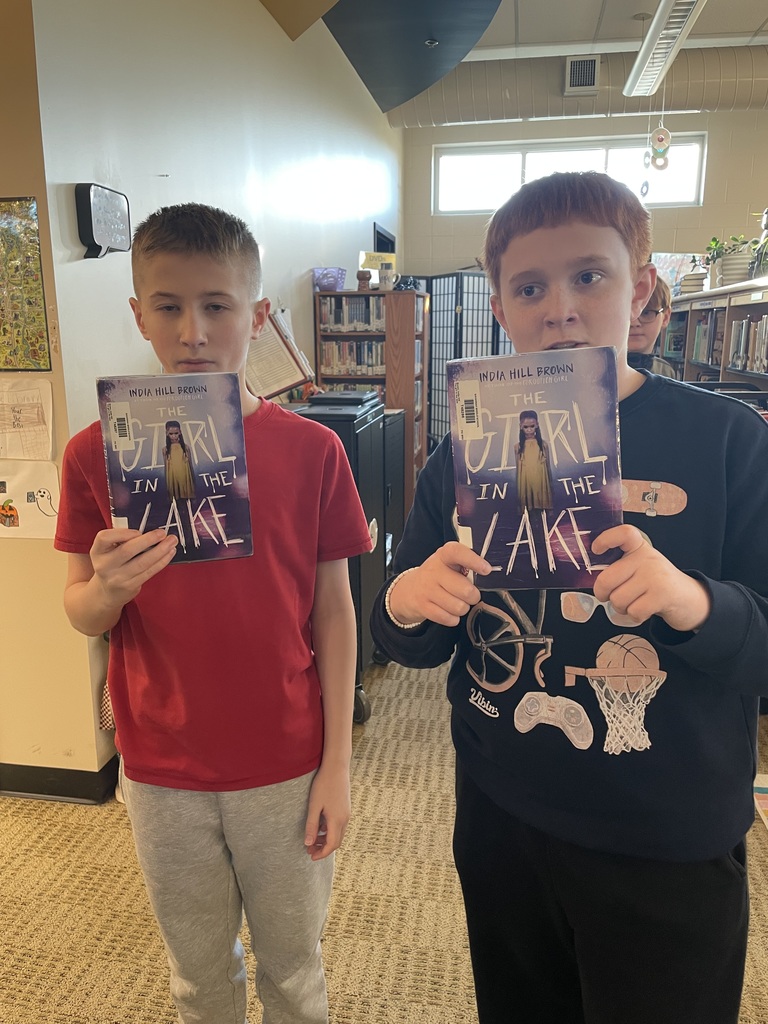 Two middle school boys hold copies of The Girl in the Lake in the library.