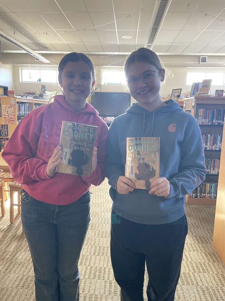 Two middle school girls in the library hold copies of Diamonds in the Shadow.