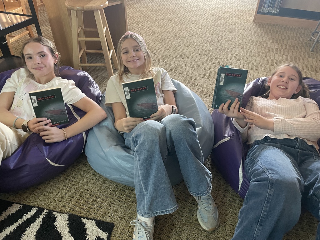 Three middle school girls sit on bean bags in the library holding copies of Red Kayak.