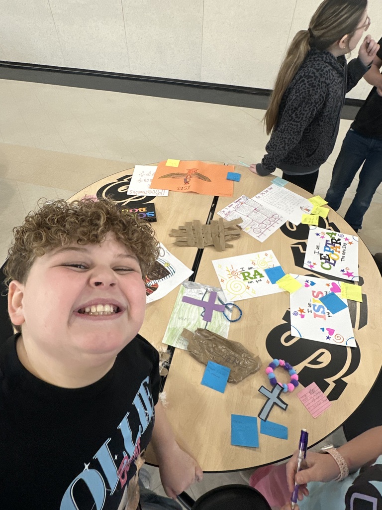 A smiling student stands beside handmade Egyptian-themed projects displayed on a table.