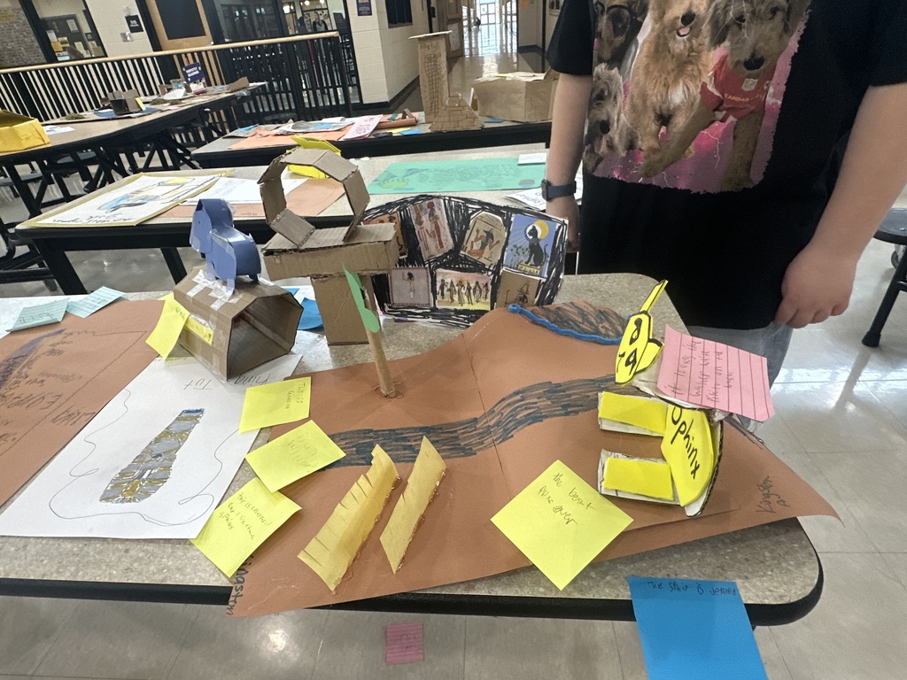 Student projects about Ancient Egypt displayed on a cafeteria table, including drawings, notes, and artifact replicas.