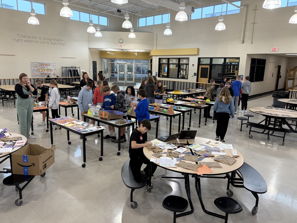 Students walking through rows of tables filled with Ancient Egypt projects in a large school commons area.