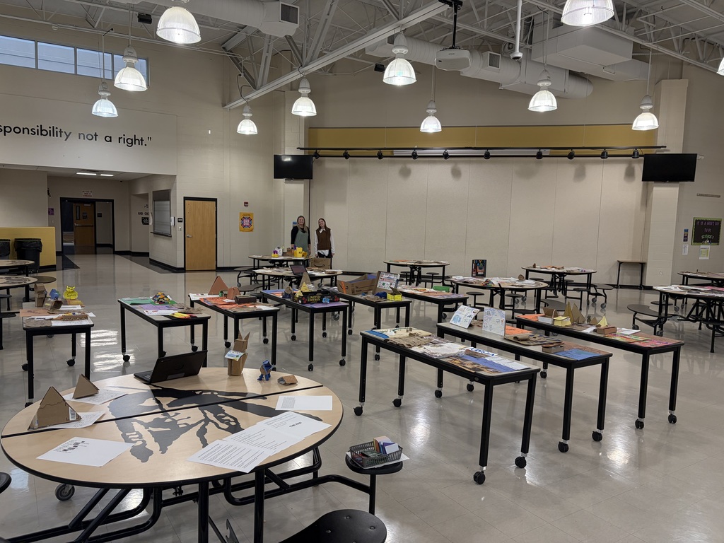 Wide view of a school commons filled with tables displaying student projects from an Ancient Egypt unit.
