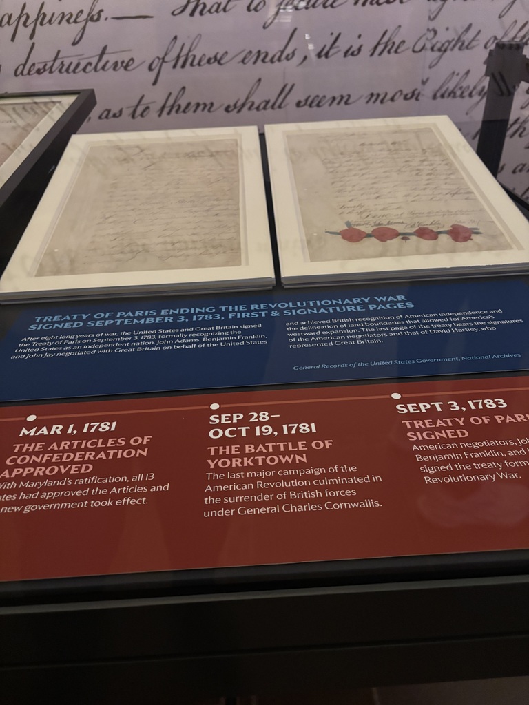 A museum exhibit shows pages from the Treaty of Paris with text explaining key Revolutionary War dates and events.