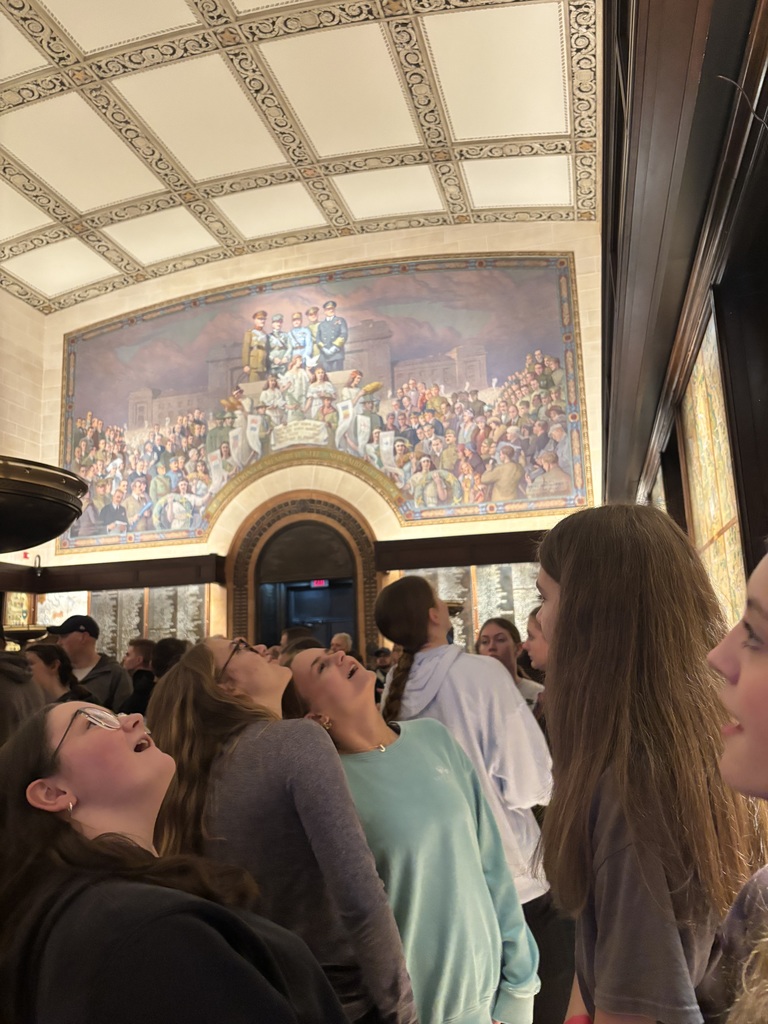 Students look up at a large mural inside the museum’s memorial hall during their field trip.