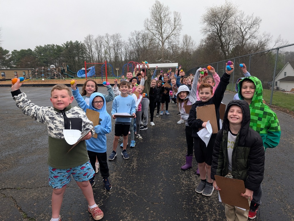 A long line of second graders outdoors holds colorful plastic eggs and clipboards during a math fact scavenger hunt.
