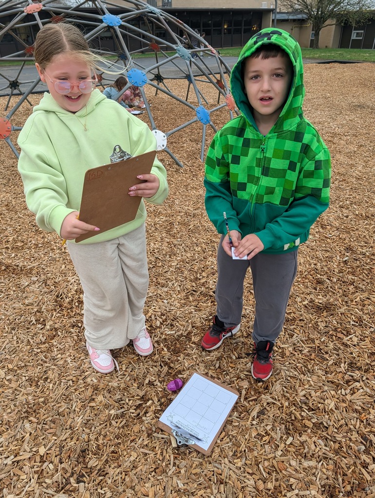 Two second graders stand on the playground with a clipboard and pencil after opening a math review egg.