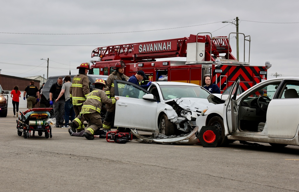 First responders assist at a staged crash scene with a damaged car during the Docudrama event.