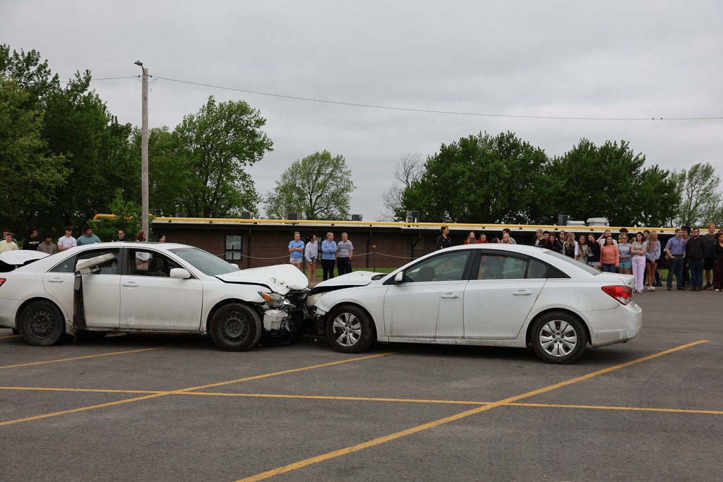 Two damaged cars staged in a crash scene as students observe the Docudrama safety demonstration.
