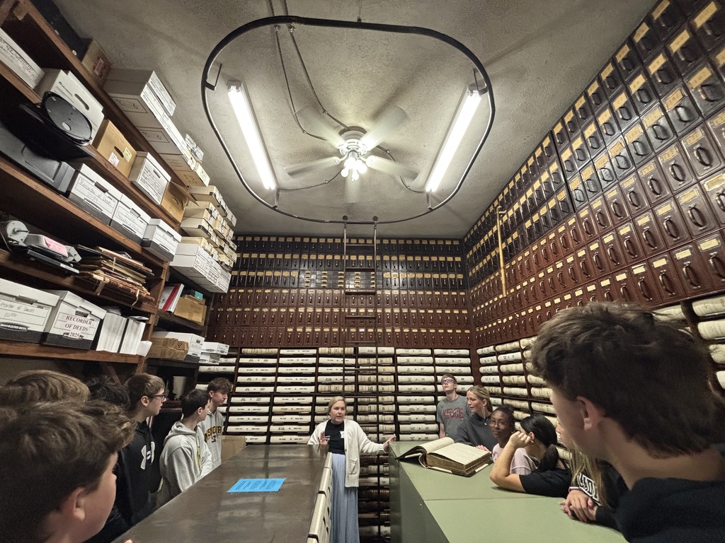 Students gather in a records room at the courthouse as a staff member explains historic books and document storage.