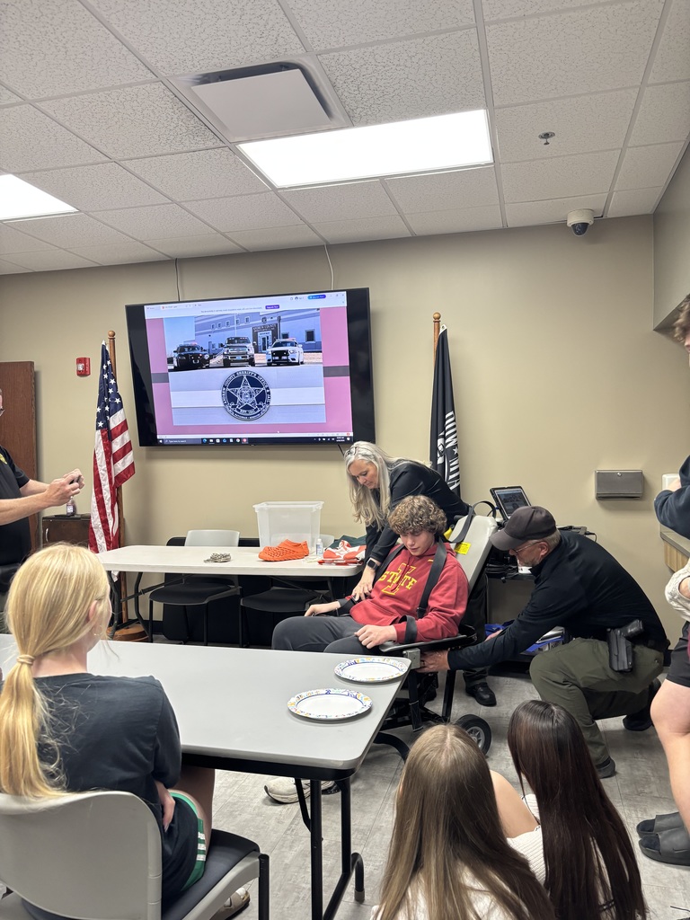 Students watch a safety demonstration inside the jail classroom as staff members secure a student volunteer into an evacuation chair.