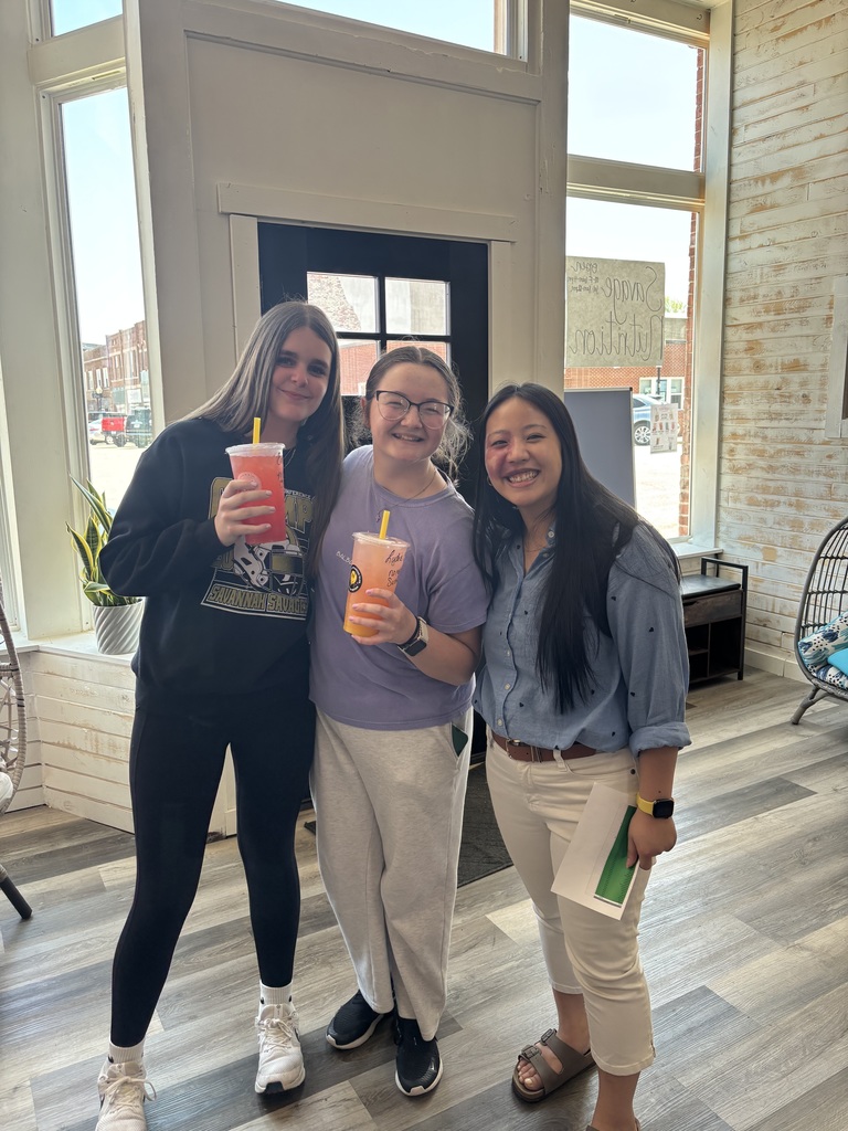 Three students pose with colorful drinks inside Savage Nutrition near the front windows.