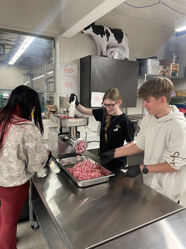 Three students work together at a meat grinder as ground pork fills a tray in the Animal and Food Science classroom.