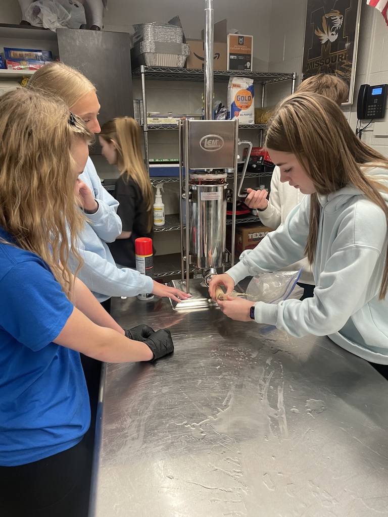 Students work at a sausage stuffer in class, filling casings on a stainless steel table during a hands-on food science activity.
