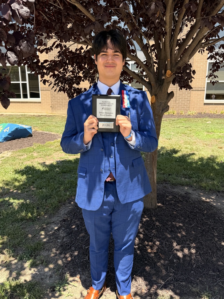William Calderwood stands outdoors in a blue suit, holding a National Speech & Debate Tournament plaque and wearing debate ribbons.