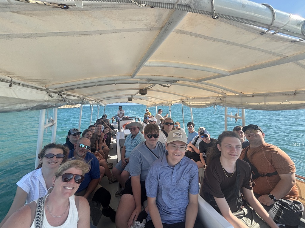 Savannah High School students and chaperones smile together on a boat with bright blue water surrounding them.