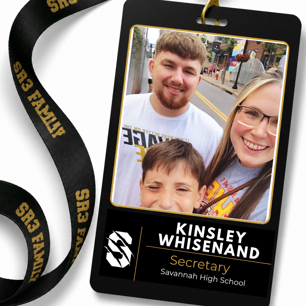 Black SR3 staff ID badge hanging from a black "SR3 Family" lanyard on a white background. The badge features a portrait of Kinsley Whisenand. Text identifies her as the Attendance Secretary at Savannah High School.