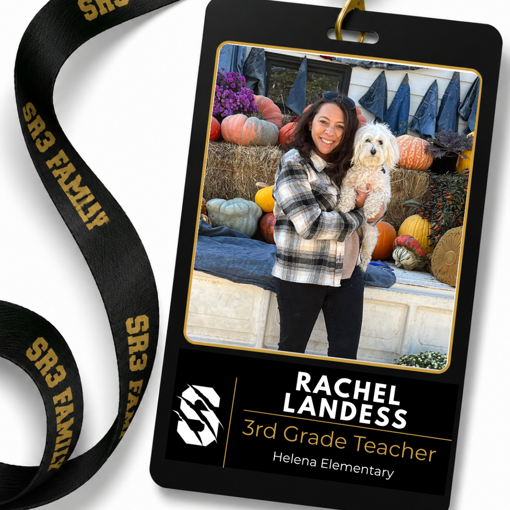 New Helena Elementary third grade teacher Rachel Landess smiles while holding a small white dog in front of a fall pumpkin display.