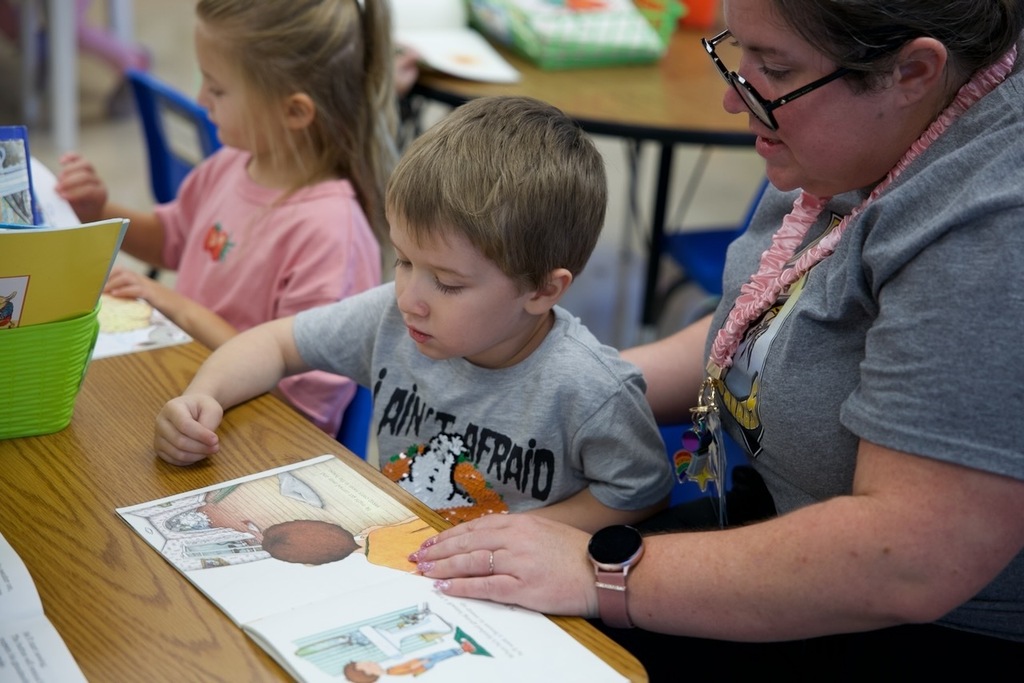 Teacher reads alongside a young student during a classroom activity.