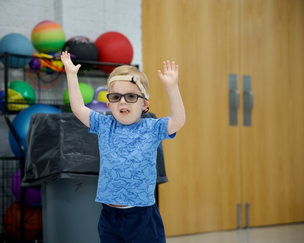 Young student raises both hands during an activity in the school gym.