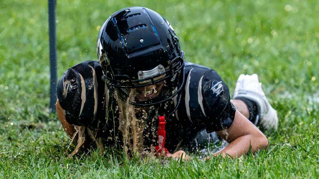 Soaked middle school football player smiles while lying in a puddle after sliding through the wet grass.