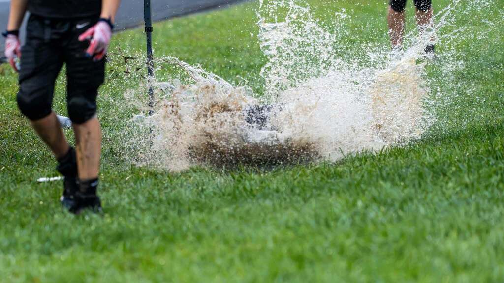 Middle school football player hits a large puddle, creating a huge splash of muddy water.
